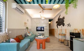 A modern living room with a sofa, ottoman, ceiling fan, TV, and a kitchen area with a fridge and stove. - light of the dawn (Liuqiu)