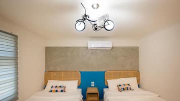 A room with two beds, a small table, and an air conditioning unit.