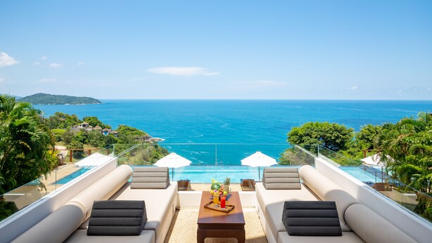 A balcony with a view of the ocean, a pool, and lounge seating.
