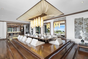 A spacious dining area with a long wooden table set for a meal, a large chandelier, and a view of the outdoors.