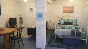 A room with a white brick wall, a bed with patterned bedding, a desk with a computer, and a chair. - Your Stay in Rye (Rye)