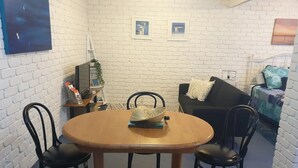 A compact living space with a round wooden table, four black chairs, a black sofa, and a small bookshelf. - Your Stay in Rye (Rye)