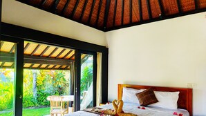 A bedroom with a bed, a wooden headboard, and a view of a garden through a glass door. - 3BR Villa Queen With Stunning Rice Field (Blahbatuh)