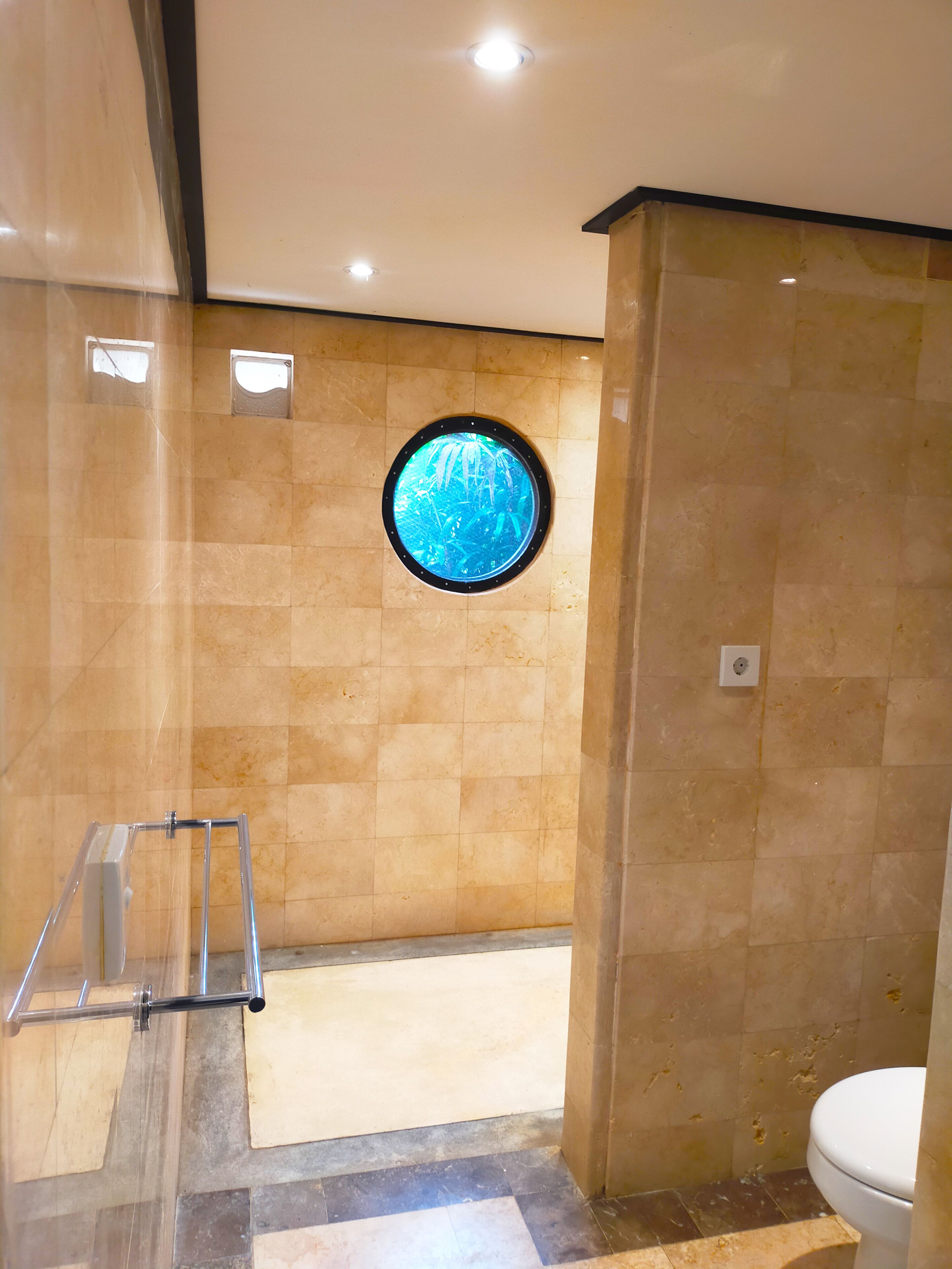 A bathroom with a round window, tiled walls, and a toilet.