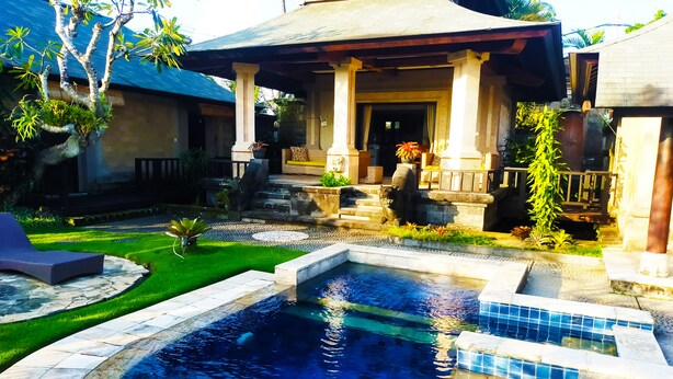A swimming pool with a stone border, a covered patio, and a stone statue. - 3BR Villa Queen With Stunning Rice Field (Blahbatuh)