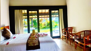 A hotel room with a bed, a chair, and a view of a garden through large windows. - 3BR Villa Queen With Stunning Rice Field (Blahbatuh)