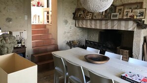 Ein rustikaler Innenraum mit Steinwand, Kamin, Esstisch mit Stühlen und einer Pendelleuchte.