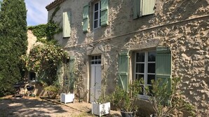 Ein rustikales Steinhaus mit grünen Fensterläden, einer Schotterauffahrt und Kübelpflanzen.