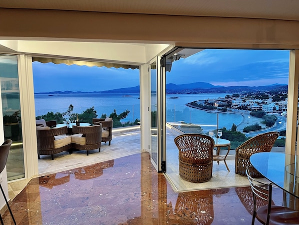 A balcony with wicker furniture, a glass table, and a view of the sea and town. - Luxurious 2-bed Seaside Apartment in Saronida (Saronikos)
