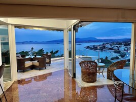 Un balcón con mobiliario de mimbre, una mesa de vidrio y vistas al mar y a la ciudad.