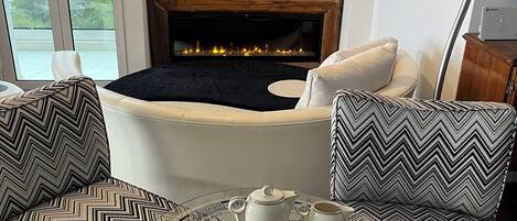 Ein Wohnzimmer mit Kamin, Fernseher und rundem Couchtisch mit einer Teekanne und Bechern.