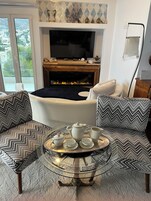 A living room with a fireplace, a television, and a round coffee table with a tray of tea set.