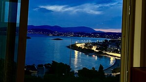 A view from a room with a large window overlooking a body of water, a distant cityscape, and mountains. - Luxurious 2-bed Seaside Apartment in Saronida (Saronikos)