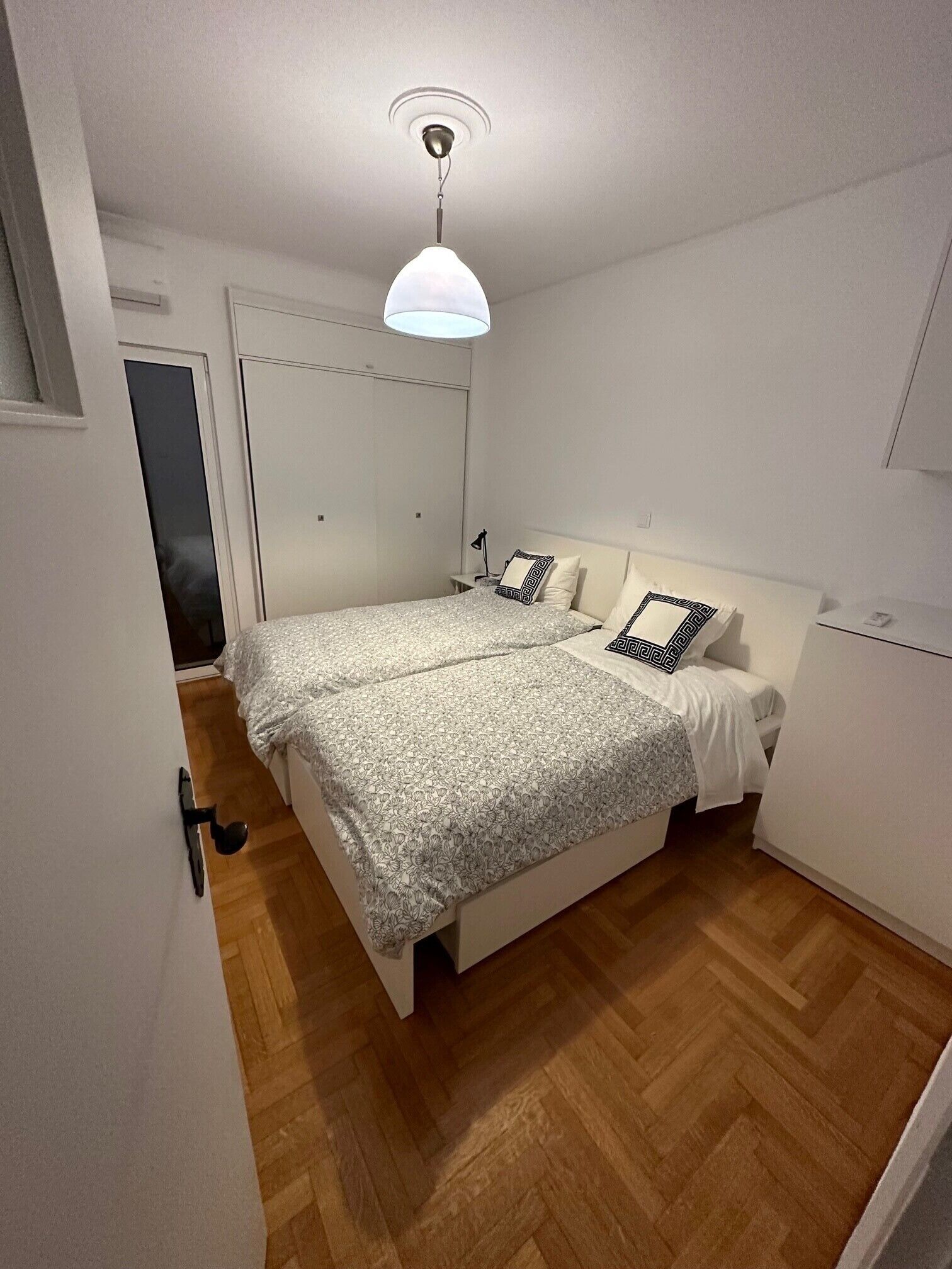 A bedroom with a bed, a bedside table, a lamp, and a wardrobe.