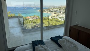 A bedroom with a large sliding glass door leading to a balcony with a view of the sea and a coastal town. - Luxurious 2-bed Seaside Apartment in Saronida (Saronikos)