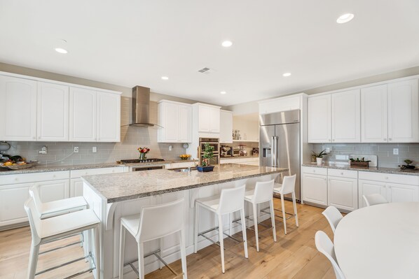 A modern kitchen with white cabinets, a central island with bar stools, a stainless steel refrigerator, and a wooden countertop backsplash.