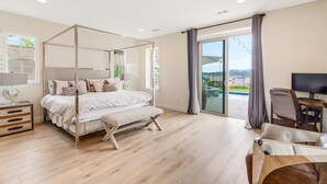 A modern bedroom with a four-poster bed, a desk with a chair, and a large window with curtains. - Resort-like residence with pool, jacuzzi, sauna, ocean breeze & amazing sunsets (Mission Viejo)
