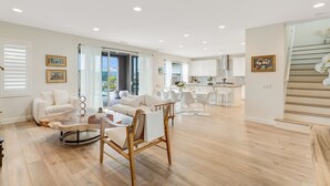A spacious living area with a wooden coffee table, white sofas, and a dining area with white chairs. - Resort-like residence with pool, jacuzzi, sauna, ocean breeze & amazing sunsets (Mission Viejo)
