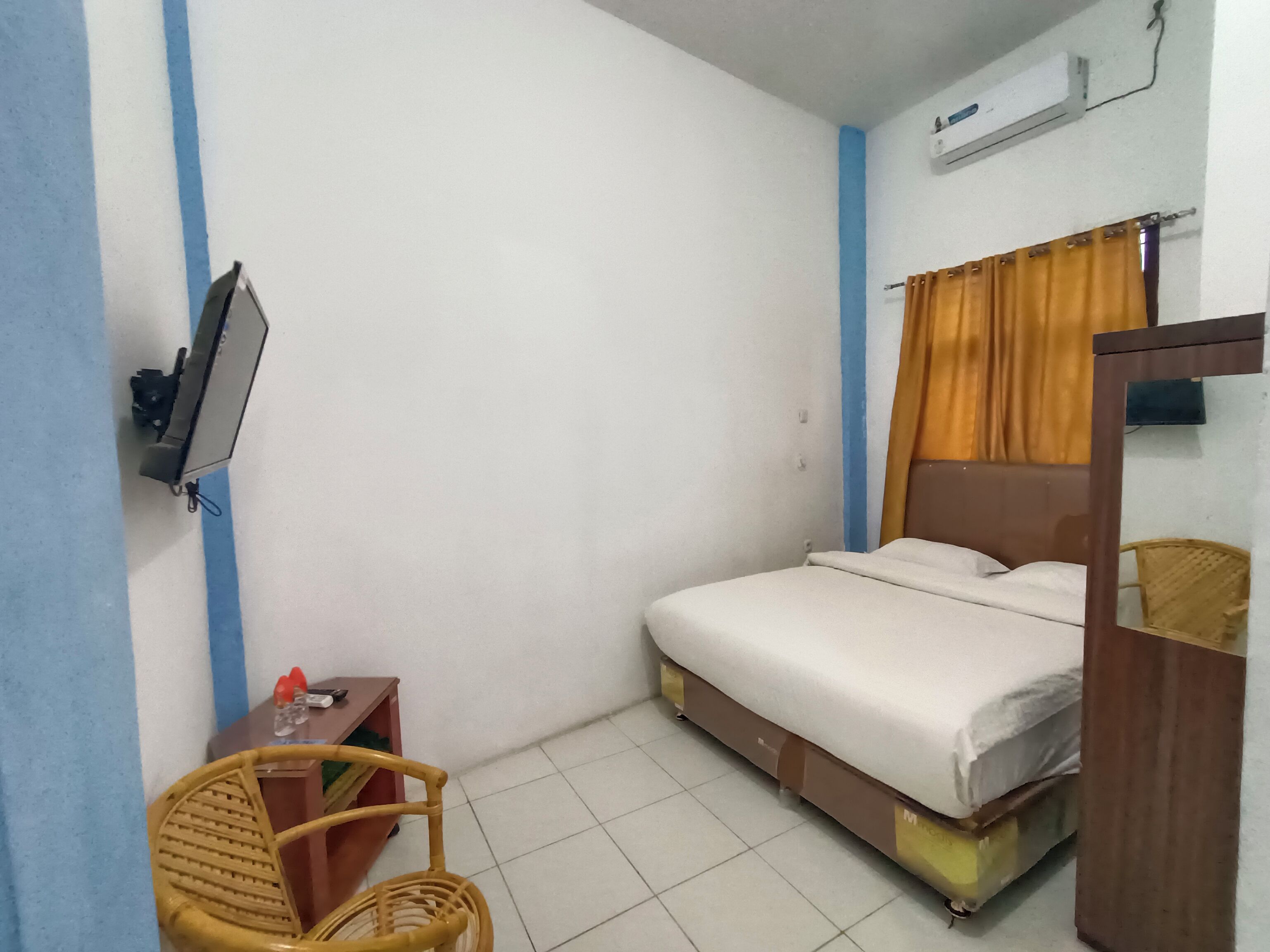 A small, clean room with a single bed, a wooden chair, a small table, and a TV mounted on the wall.