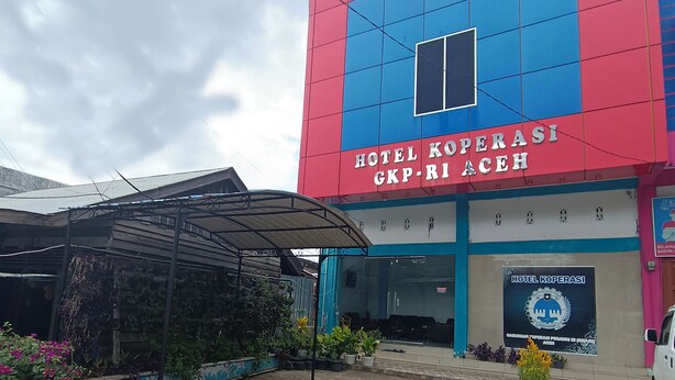 Un hôtel dont la façade rouge et bleue est particulièrement remarquable, avec une entrée couverte et une enseigne indiquant qu’il s’agit de l’hôtel Koperasih GKP-RI Aceh.