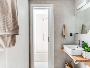 Ein modernes Badezimmer mit einem weißen Waschbecken, einem Spiegel und einem Handtuch an der Wand.