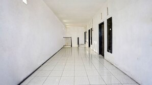 A long, narrow hallway with white walls and a tiled floor, leading to a door at the end. - Hotel O Kost Umik Sidoarjo Syariah (Sidoarjo)