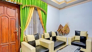A room with a wooden door, green and yellow curtains, beige and black sofas, a patterned coffee table, and a decorative wall piece. - Hotel O Kost Umik Sidoarjo Syariah (Sidoarjo)