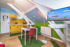 A room with a dining area, a television displaying a video game, and a kitchen area.