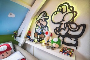 A room with a white shelf displaying Mario and Luigi plush toys, a Mario-themed pillow, and a Mario-themed wall decoration.