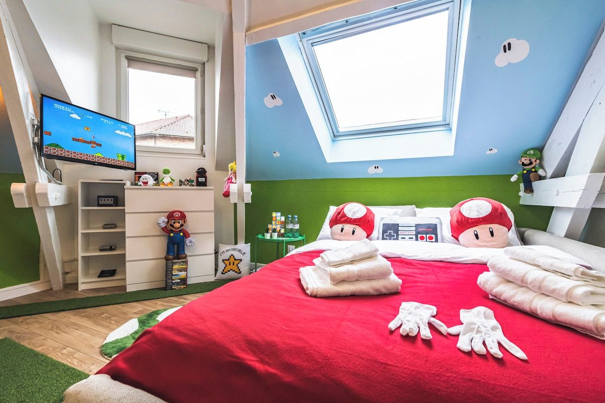 Une chambre à coucher décorée sur le thème de Nintendo, avec des peluches de Mario et un coussin à l’effigie de Mario.