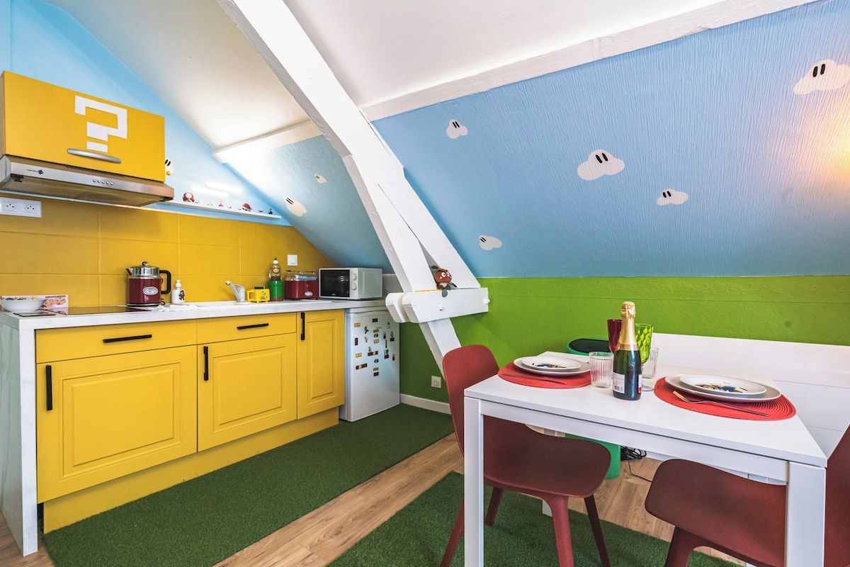 Een keuken met gele kastjes, een wit aanrechtblad en een eethoek met een witte tafel en rode stoelen.