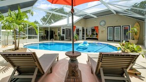 Un espace piscine avec des chaises longues, un parasol rouge et une fontaine décorative.