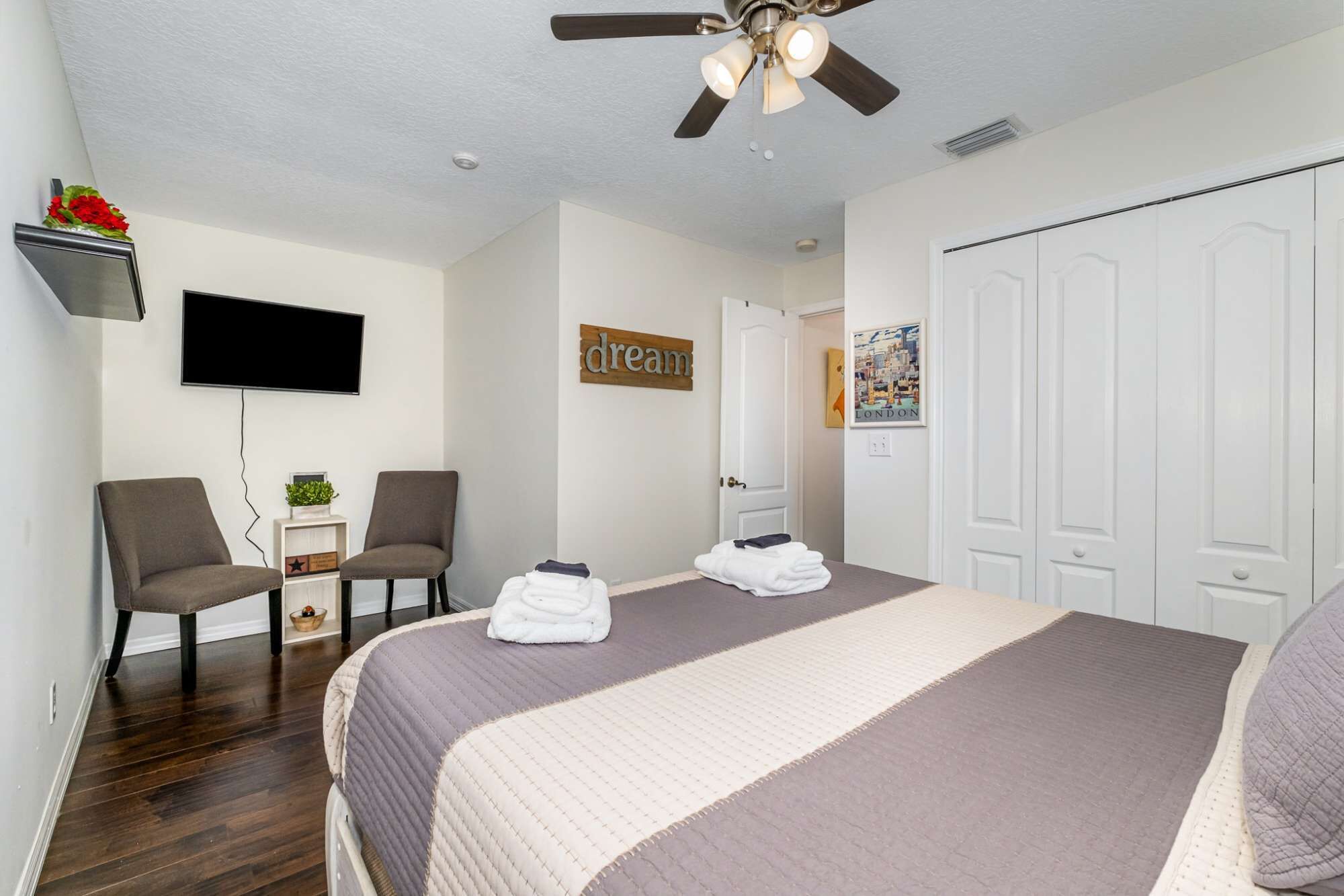 Une chambre d’hôtel avec un lit, deux chaises, un téléviseur, un ventilateur de plafond et une porte.