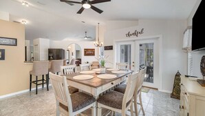 Un coin repas avec une table en bois, des chaises blanches et un ventilateur de plafond.