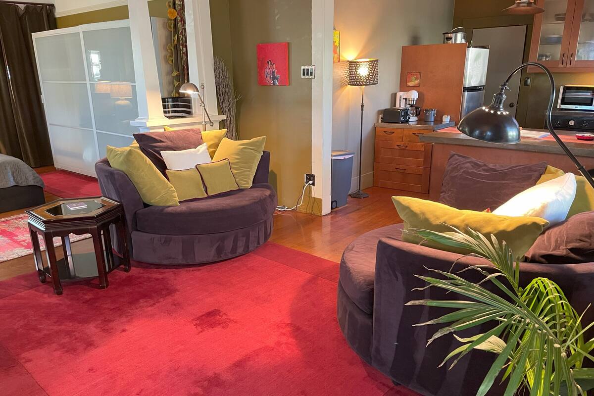 A living room with a red carpet, a sofa set, a coffee machine, and a kitchen area.
