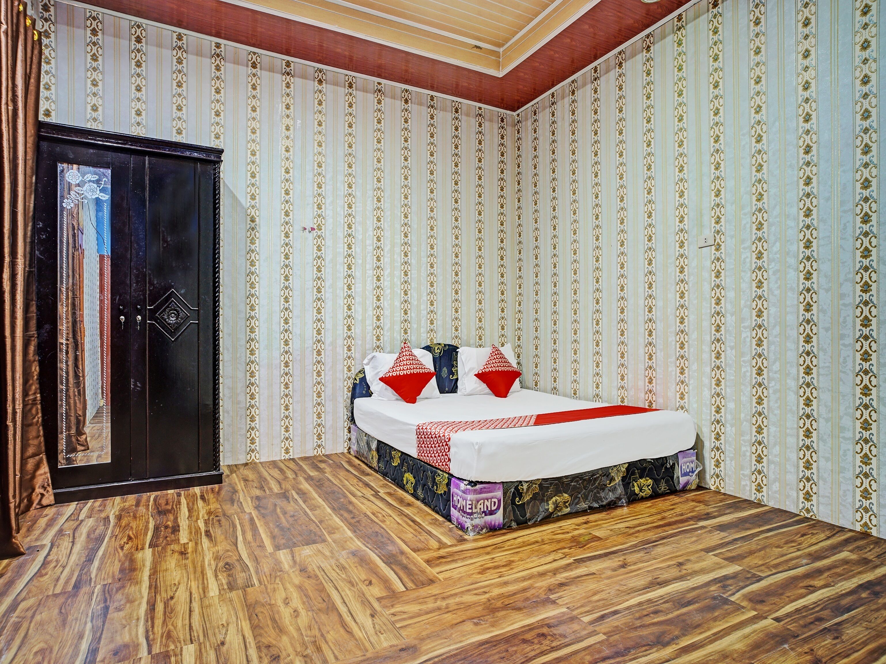 A bedroom with a wooden floor, a bed with a patterned mattress, and striped wallpaper.