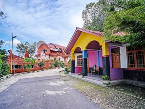 A colorful building with a red roof, a statue, and a paved area with plants. - Hotel O Taman Wisata Iman Ii Near Taman Wisata Iman Sitinjo (Kota Sidikalang)