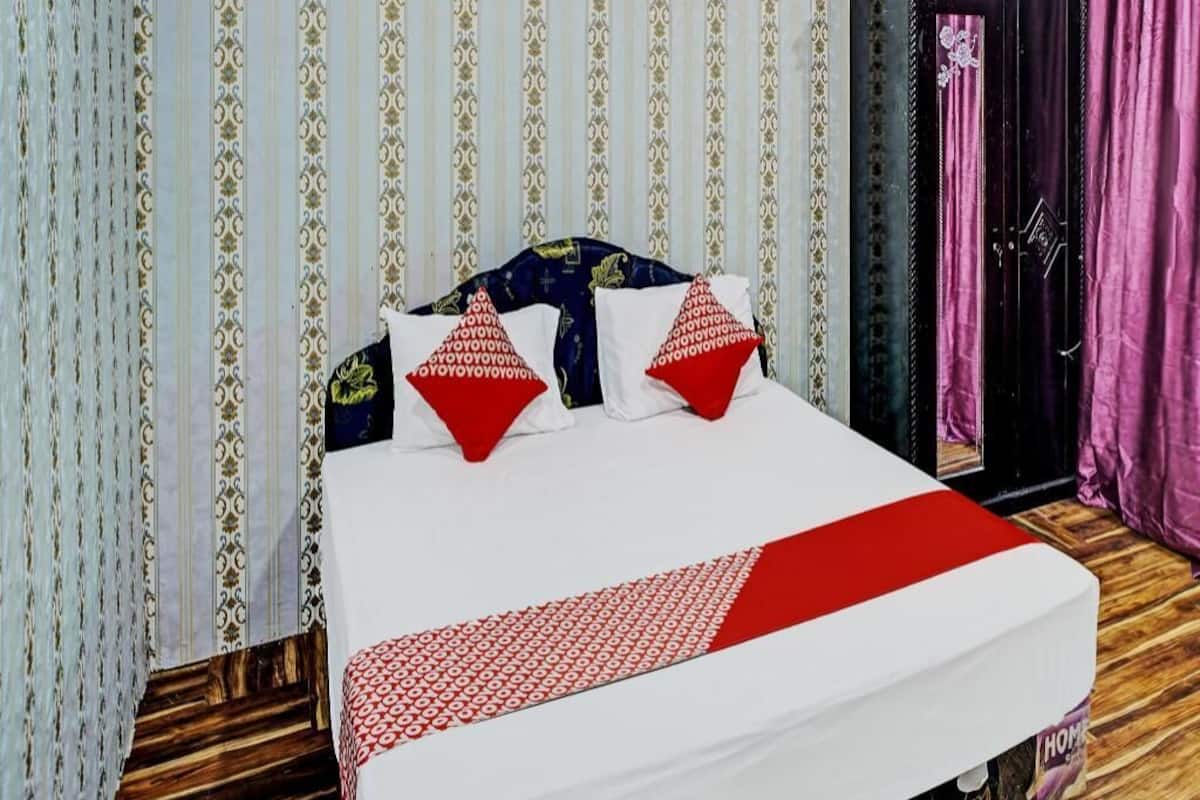 Ein Bett mit weißroter Bettdecke, zwei rote Kissen und ein Kopfteil mit dunkelblauem und goldenem Muster.