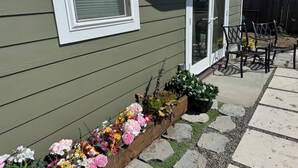 A house with a green exterior, a wooden planter with flowers, and a patio with chairs and a table. - Unobstructed ocean views in a cozy setting (Dillon Beach)