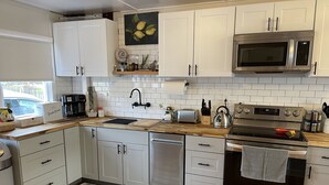 A modern kitchen with white cabinets, a stainless steel microwave, an oven, and a sink. - Unobstructed ocean views in a cozy setting (Dillon Beach)
