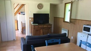 A compact living space with a sofa, a TV, a dining table, and a microwave.