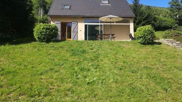A single-story house with a sloped roof, a small attached garage, and a patio area with a table and umbrella.