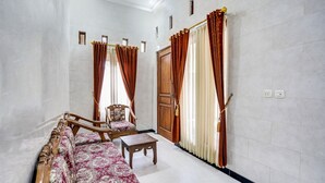 A room with a sofa, a chair, a small table, and a wooden door. - OYO Life 91893 Kost Jeje Syariah (Surabaya)