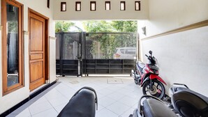 A clean, tiled entrance area with a closed gate, a red motorcycle, and a bench. - OYO Life 91893 Kost Jeje Syariah (Surabaya)