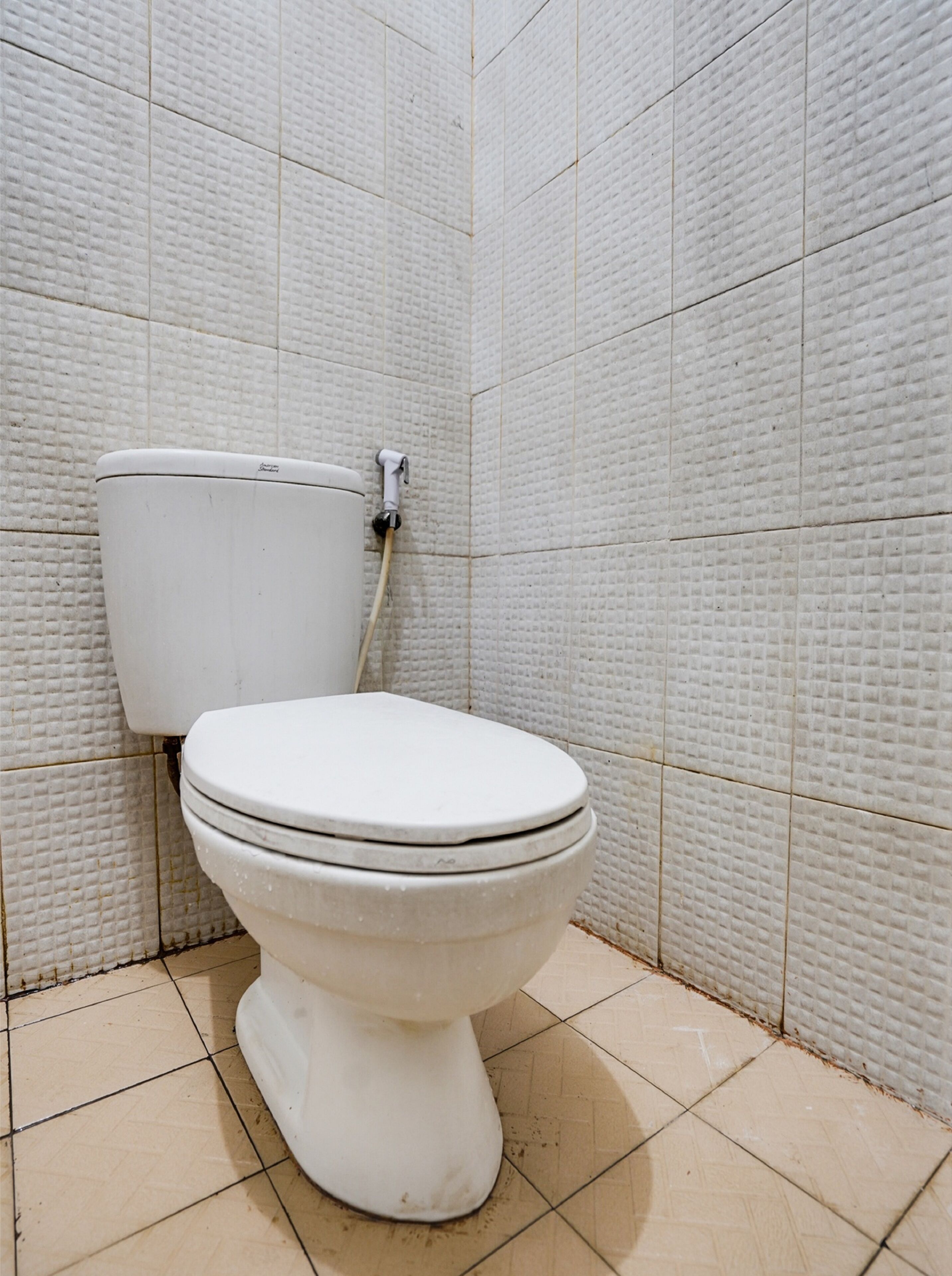 Un inodoro en un baño con baldosas blancas con textura en las paredes y el suelo.