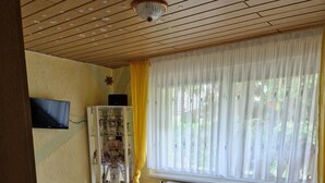A bedroom with a wooden bed, a television mounted on the wall, a radiator, and a window with curtains. - Auszeit in Ruhiger Lage (Schönfeld)