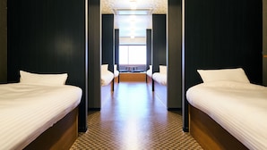Une chambre d’hôtel avec deux lits simples, une petite table et une fenêtre laissant entrer la lumière naturelle.