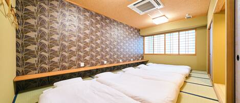Una habitación tradicional japonesa con suelo de tatami, un bajo cabecero de madera y una puerta corredera de shoji.