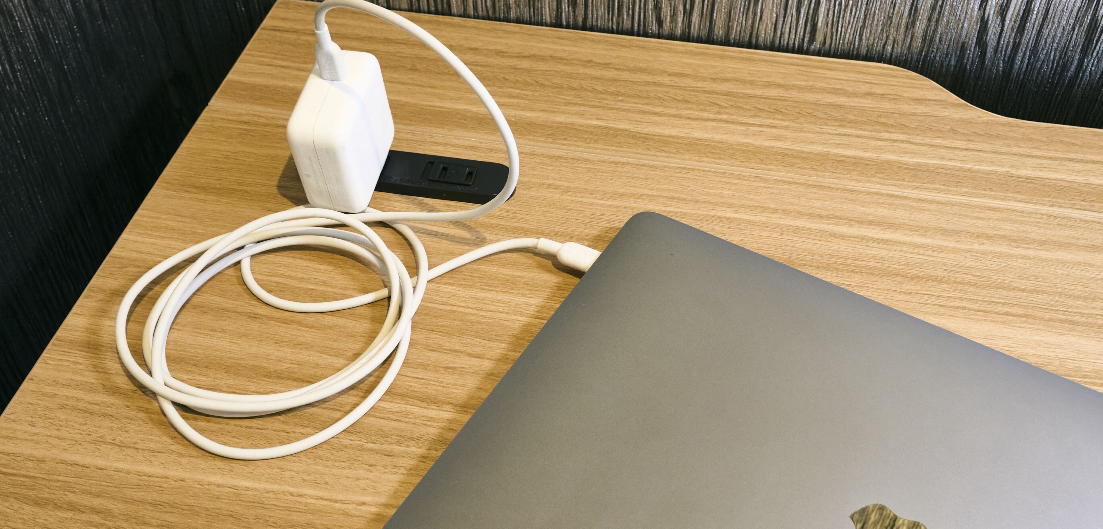 Una computadora portátil con un cable de carga blanco y un adaptador de corriente sobre una mesa de madera.