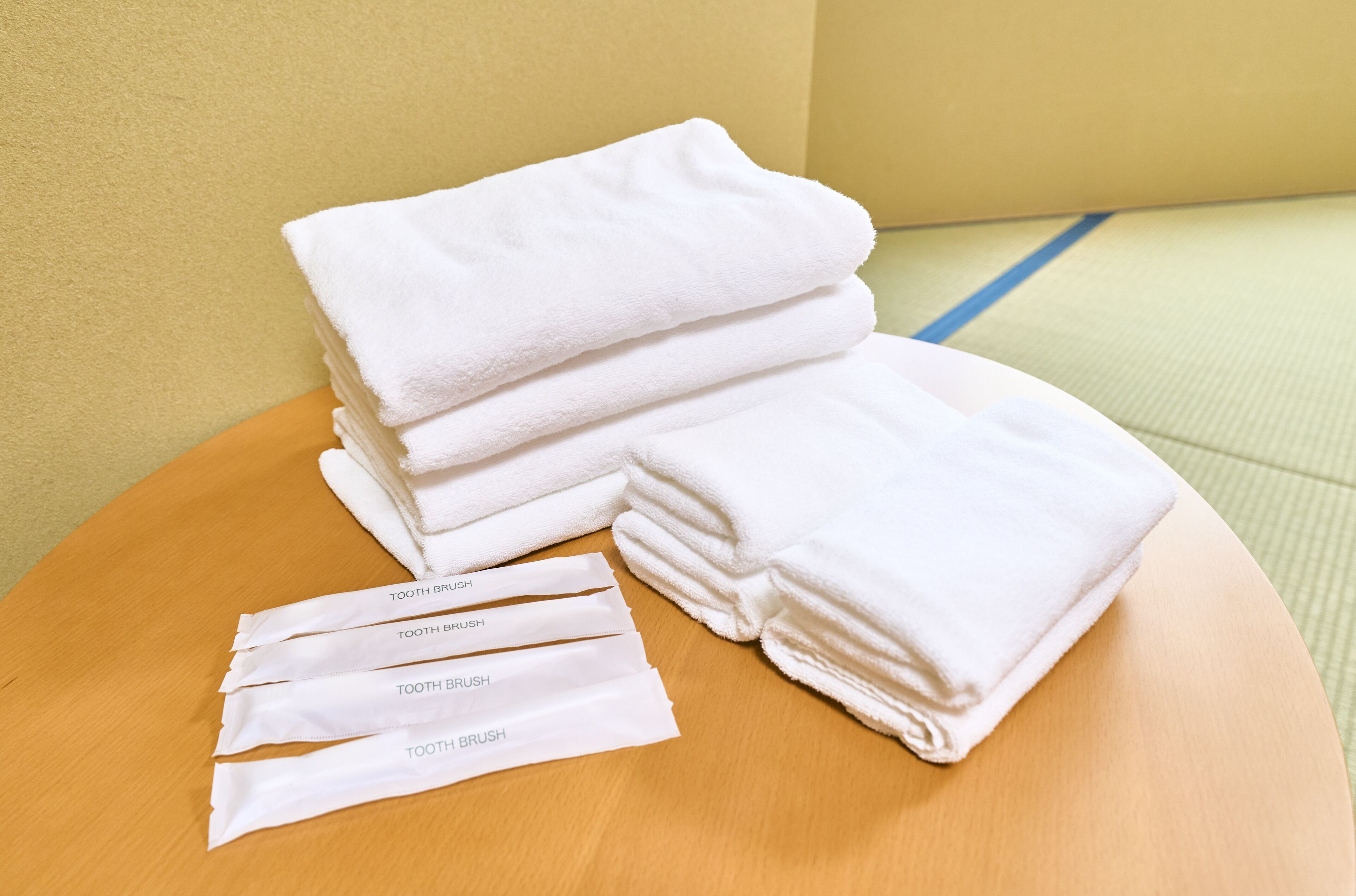 A stack of white towels and four individually wrapped items labeled "TOOTH BRUSH" on a wooden surface.